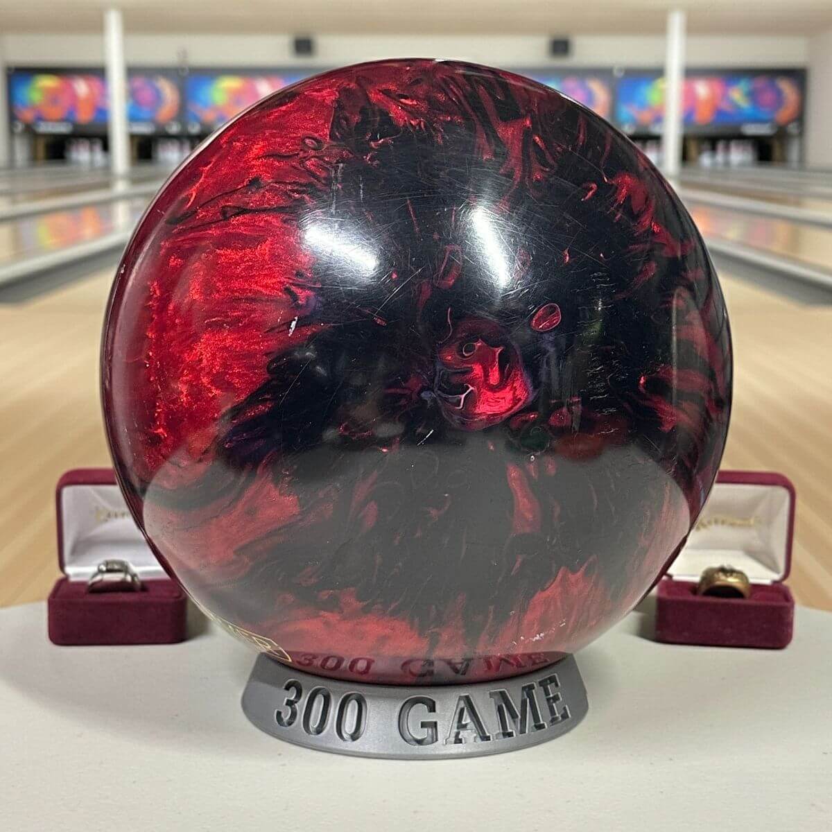 Red and black bowling ball with '300 Game' plaque in a bowling alley setting