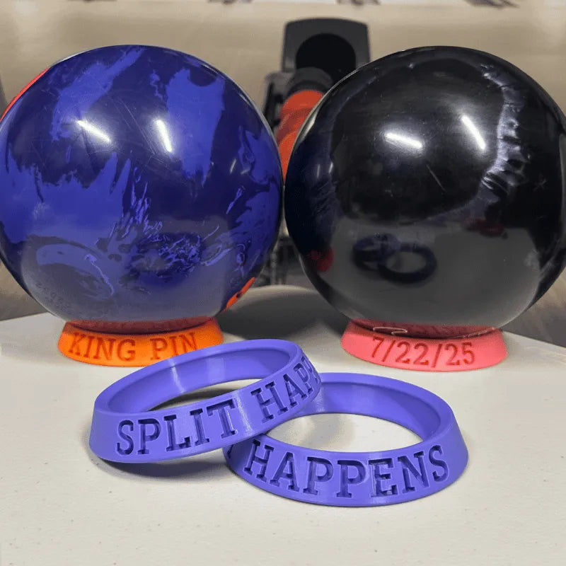 Two blue and black bowling balls with purple 'SPLIT HAPPENS' wristbands on a white surface.