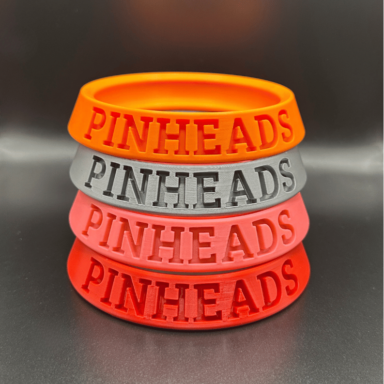 Stack of orange, gray, red, and pink wristbands with 'PINHEADS' text on a black background