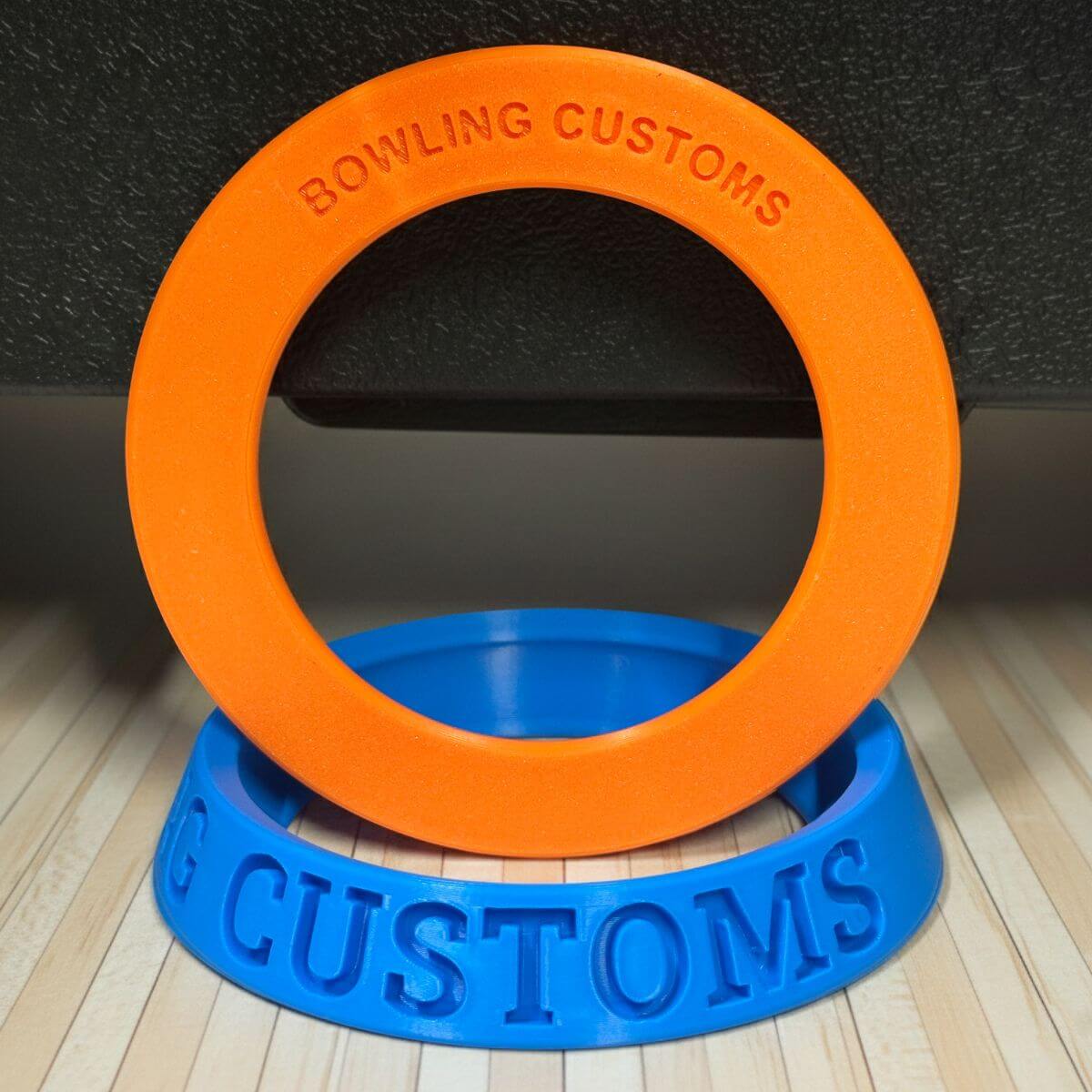Orange and blue ring-shaped object with 'Bowling Customs' branding on a dark background.