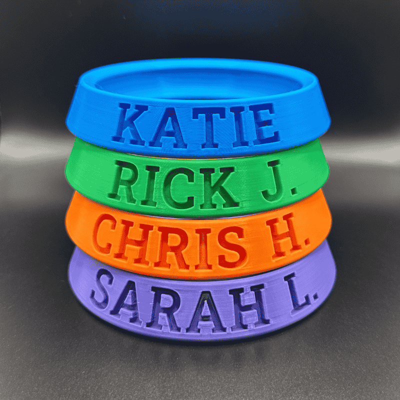 Stack of colorful silicone wristbands with embossed names on a dark background